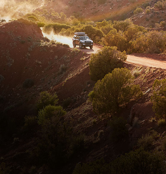 A sport utility vehicle driving down a dirt road in the mountains