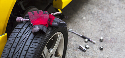 Car maintenance safety tips with work gloves and proper tools and tire off yellow car