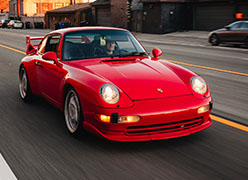 A red porsche is driving down a city street