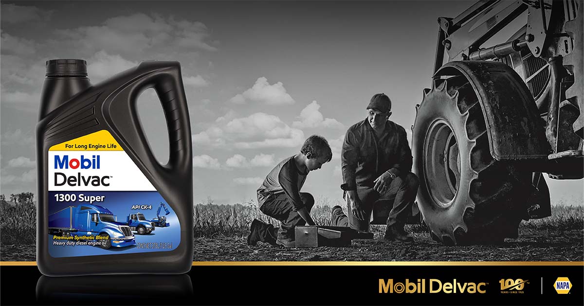 A father and son kneel next to a large farm tractor as the boy looks through a toolbox.