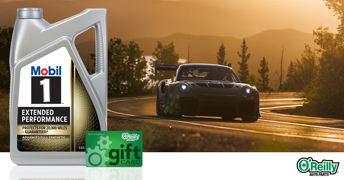 a race car, driving toward the camera, comes around a tight turn on a scenic stretch of highway.