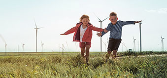 Children playing in grass field with wind turbines in background