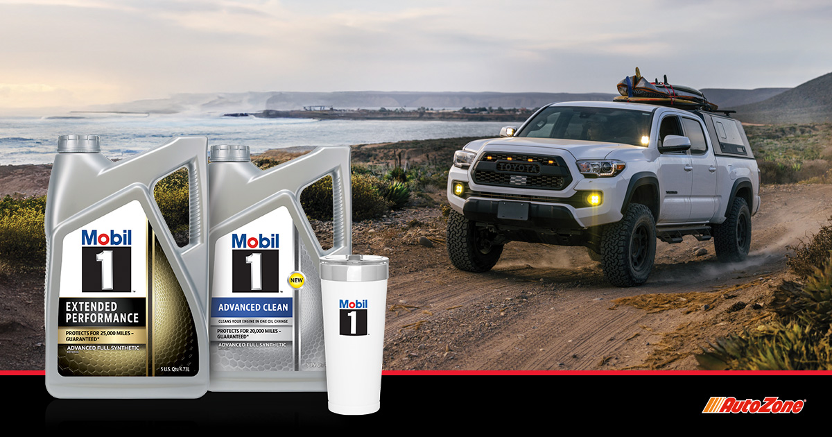 A pickup truck driving on a dirt road with water in the background. Two Mobil 1 bottles and a tumbler sit in the foreground.