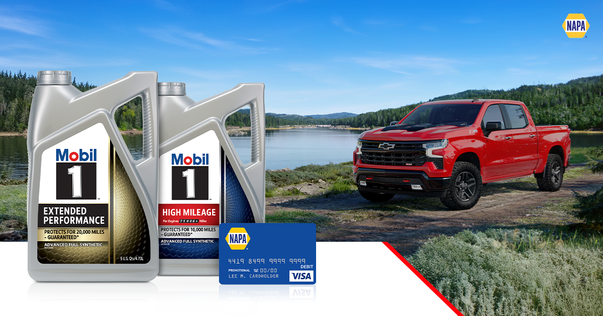 A red Chevy truck drives on a dirt and gravel road alongside a river, with lush evergreen trees lining both sides and extending all the way to the horizon.