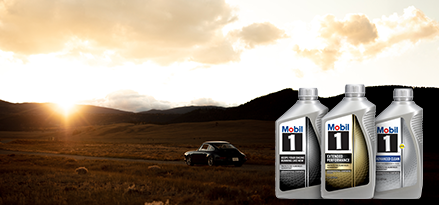 A car drives along a rural road at sunset with distant sunset. In the foreground there are three bottles of synthetic motor oils, the first is of Mobil 1, the second of Mobil 1 Extended Performance, and the third of Mobil 1 Advanced Clean