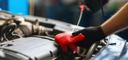 A person wearing black gloves is working under a car’s hood.