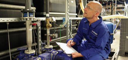 Industrial worker inspecting pump equipment and recording observations.