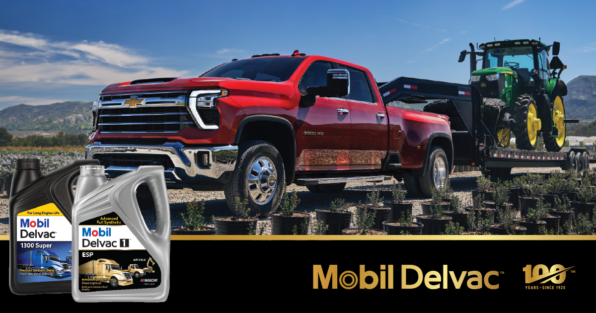 The image shows two plastic containers of Mobil Delvac motor oil. The container on the left is black with a yellow-and-blue label that reads “Mobil Delvac 1300 Super” and features a blue semi-truck illustration. The container on the right is gray with a silver-and-black label that reads “Mobil Delvac 1 ESP” and shows a gold semi-truck. Both containers have large molded handles and spouts for pouring.